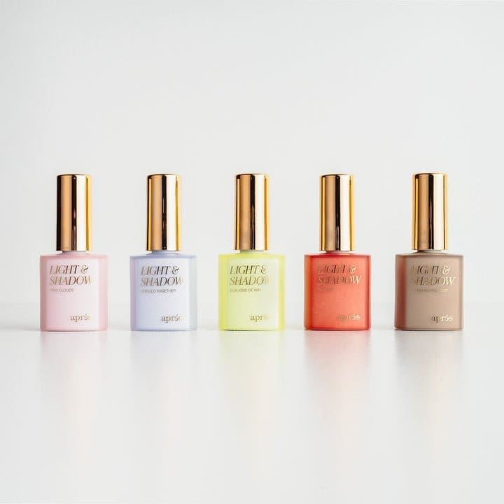 Five bottles of Apres Light & Shadow Sheer Gel Collection 10ml are arranged in a row, with colors from left to right: pink, blue, neon yellow, coral, and beige. Each 10ml bottle features a gold cap.