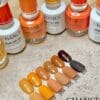 A display featuring six "CHANCE by Cre8tion" nail polish bottles and swatches from the Autumn Spice Collection showcases shades labeled 302 to 312, highlighting various tones of orange.